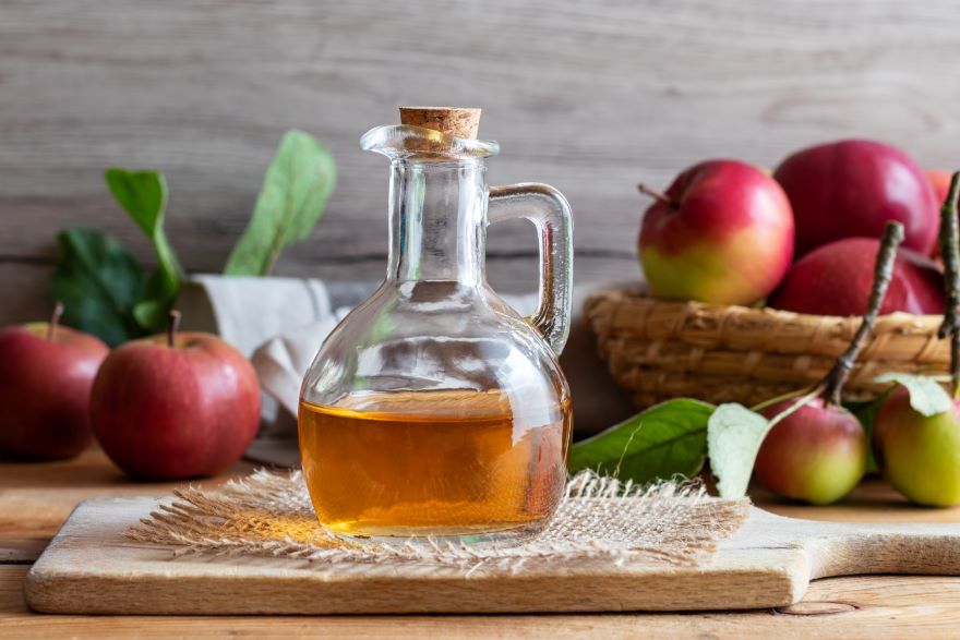 Organic apple cider vinegar in a jug with surrounded with apples