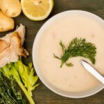 Dairy-free cream of chicken soup with celery, chicken and bread next to bowl of soup