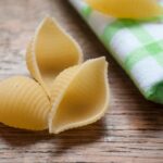 Gluten-free pasta shells x 3 on wooden background next to white and green linen