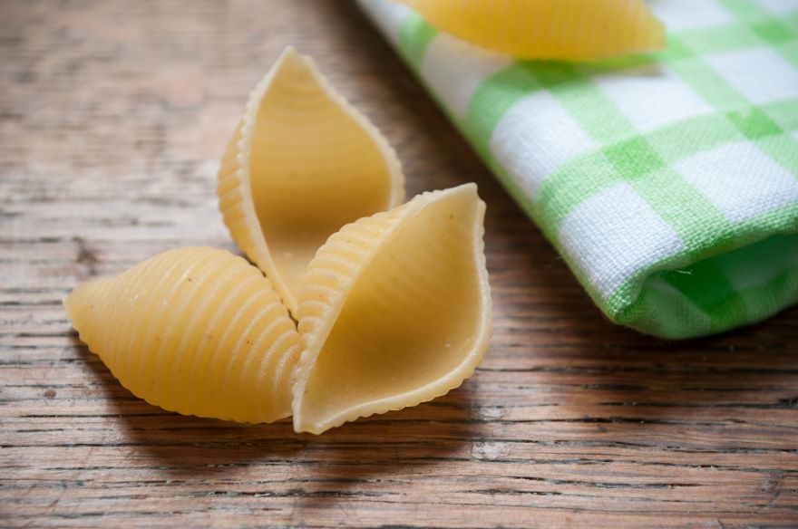 Gluten-free pasta shells x 3 on wooden background next to white and green linen