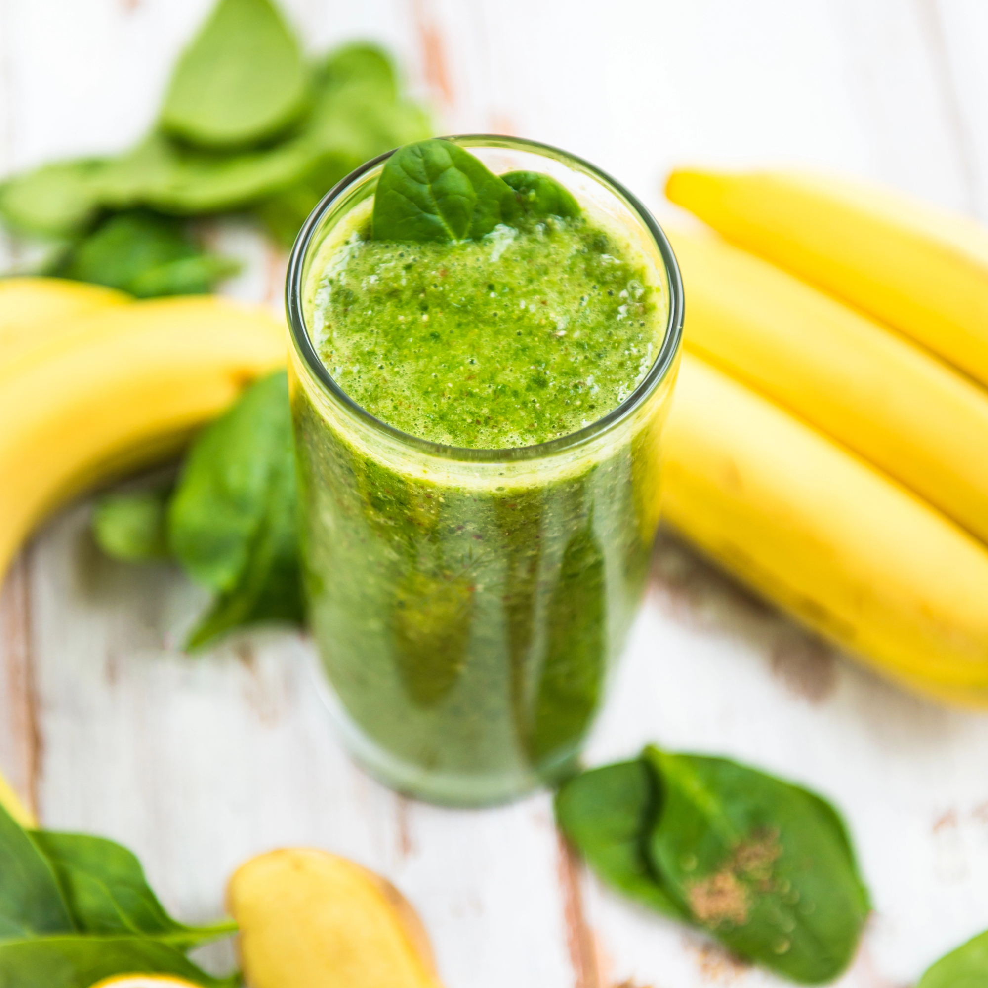 Banana spinach smoothie in a glass next to bananas