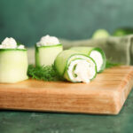 Cucumber rolls with hummus and fresh herb filling on a board
