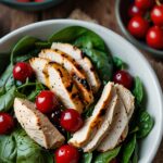 Grilled chicken salad with fresh cherries, spinach and balsamic vinegar next to bowl of tomatoes