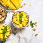 Tropical coconut oil granola with mango and macadamia nuts with two bols next to mango